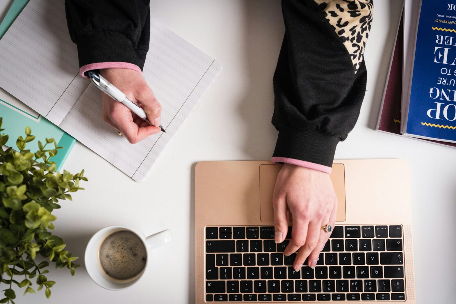 A person using a laptop while writing on a paper