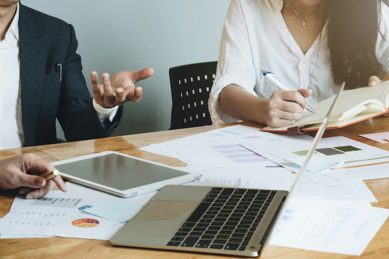 A person using a laptop and writing on a paper